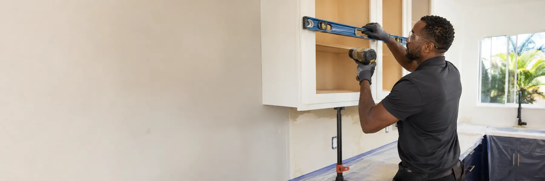 A cabinet installer leveling and fastening a kitchen wall cabinet.