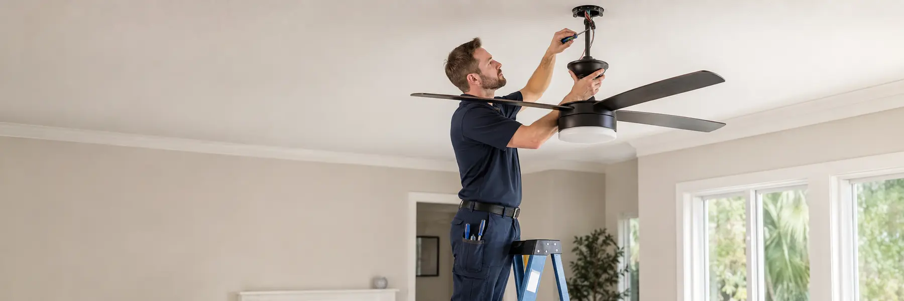 An electrician installing a ceiling fan and light at a properly supported ceiling box.