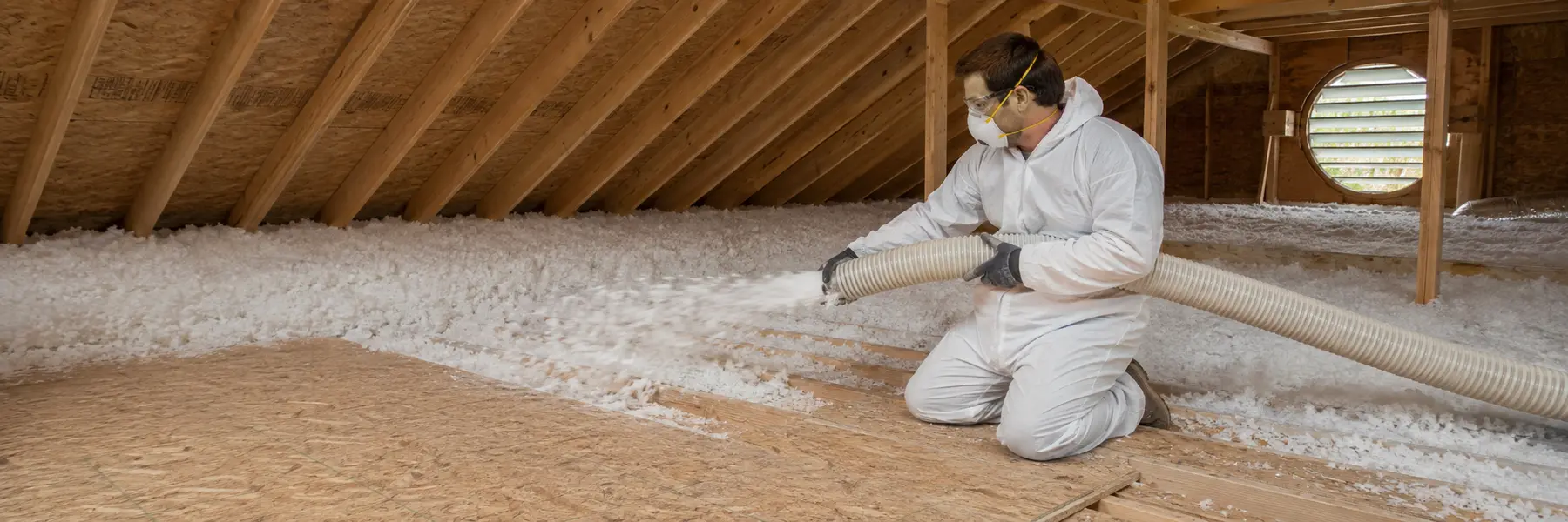 An insulation professional installing blown-in insulation across a residential attic.